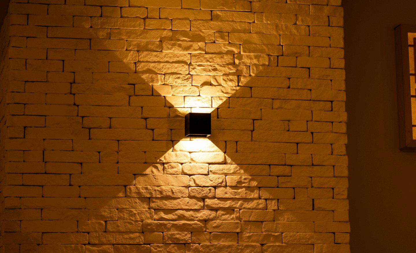 Modern black wall light casts beams on beige brick.